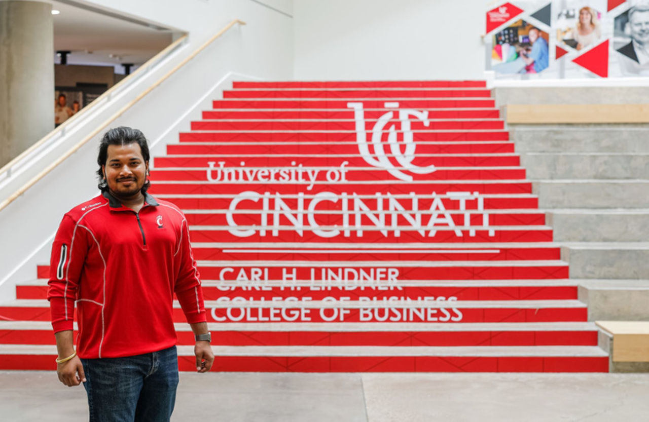Arvish Pandey standing in Lindner College of Business in front of a UC branded stairwell