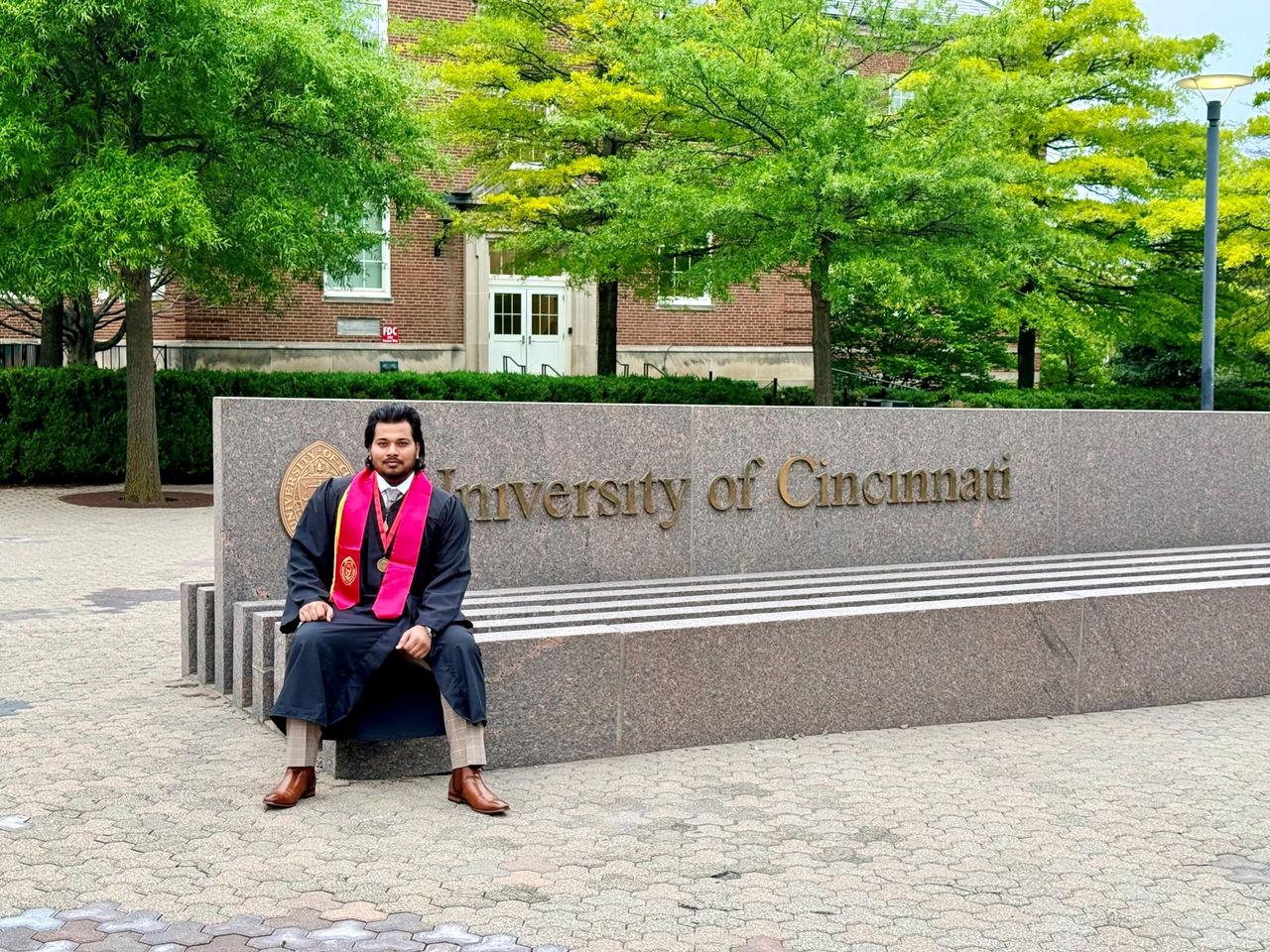 Arvish Pandey shown in cap and gown posed next to a University of Cincinnati sign on campus.