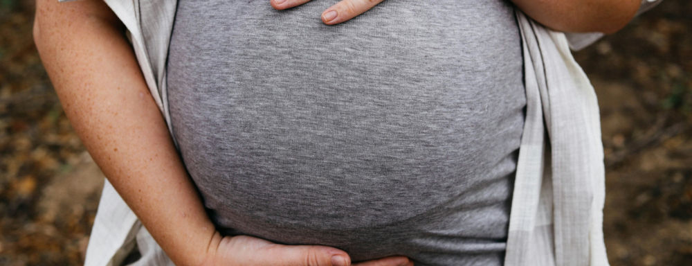 Image of woman with both hands on pregnant belly. 