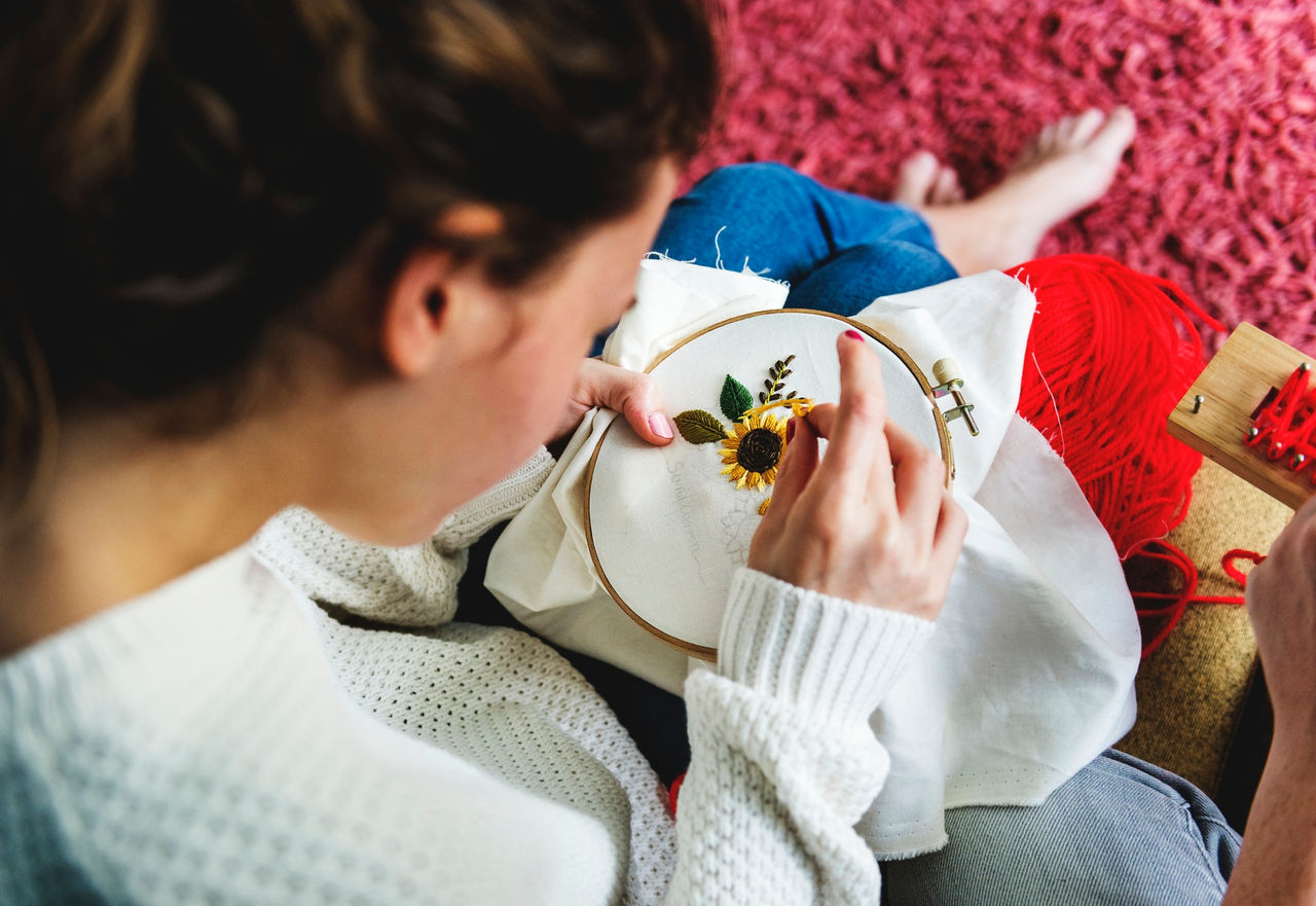 Young woman in white sweater and jeans and barefoot does needlework 