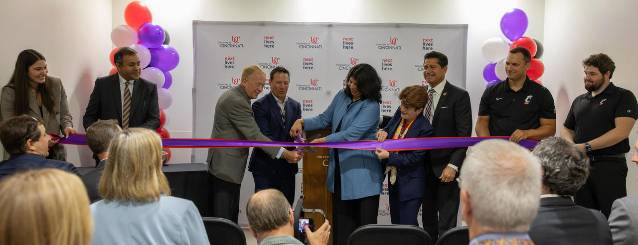 Nine people gather to hold and cut a long ribbon with large scissors 