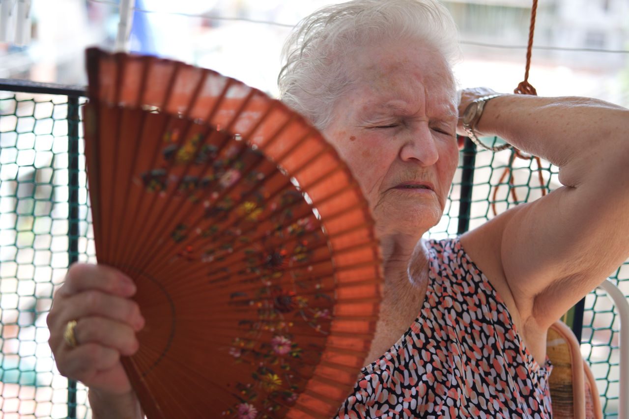 Woman in her 80s fans herself while sitting outdoors in a summer heat wave