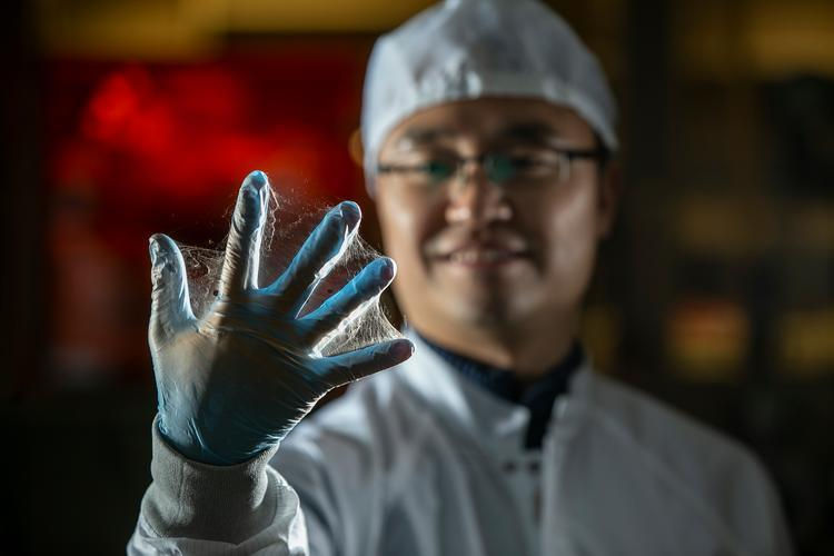 Daewoo Han wearing protective clothing holds up a gloved hand covered in nanofiber.