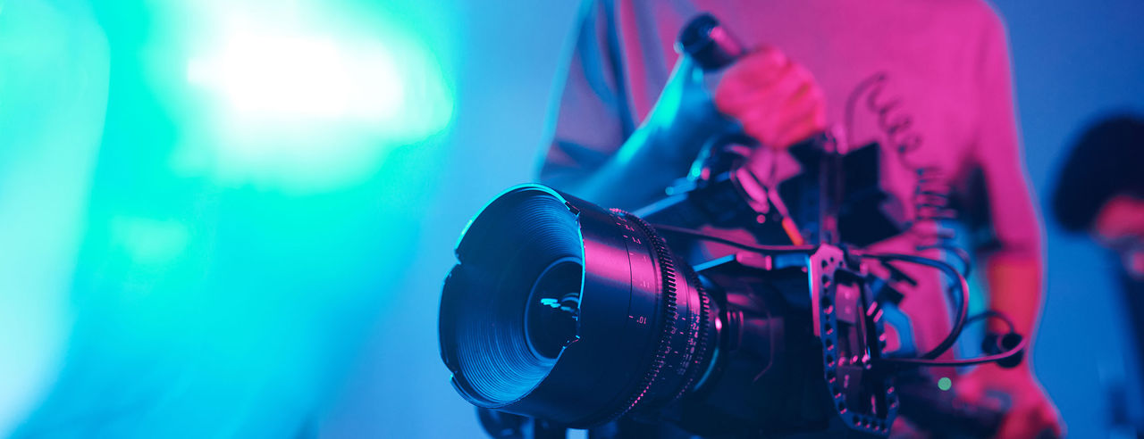 Close-up of young cameraman shooting with professional camera while making content in studio.