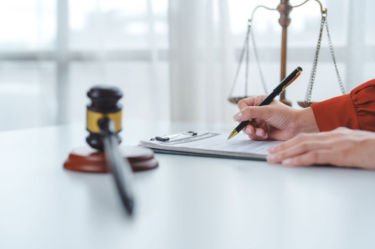 a gavel with a scale in the background and the hand of a lawyer writing on a legal pad