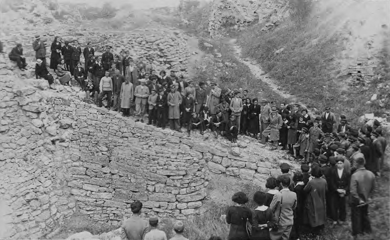 Dozens of visitors tour line up along the top of an ancient rock wall at Troy to listen to a speaker.
