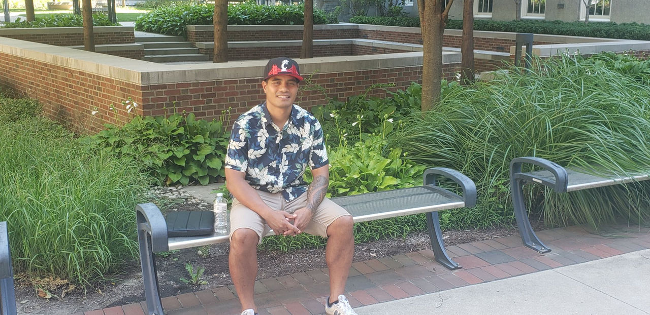 Amota Ataneka is sitting on a bench in the courtyard next to the College of Education, Criminal Justice and Human Services on the UC campus.