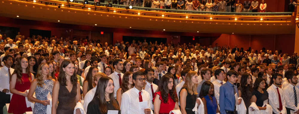 Members of the UC College of Medicine Class of 2030 standing at their seats inside the Aronoff Center
