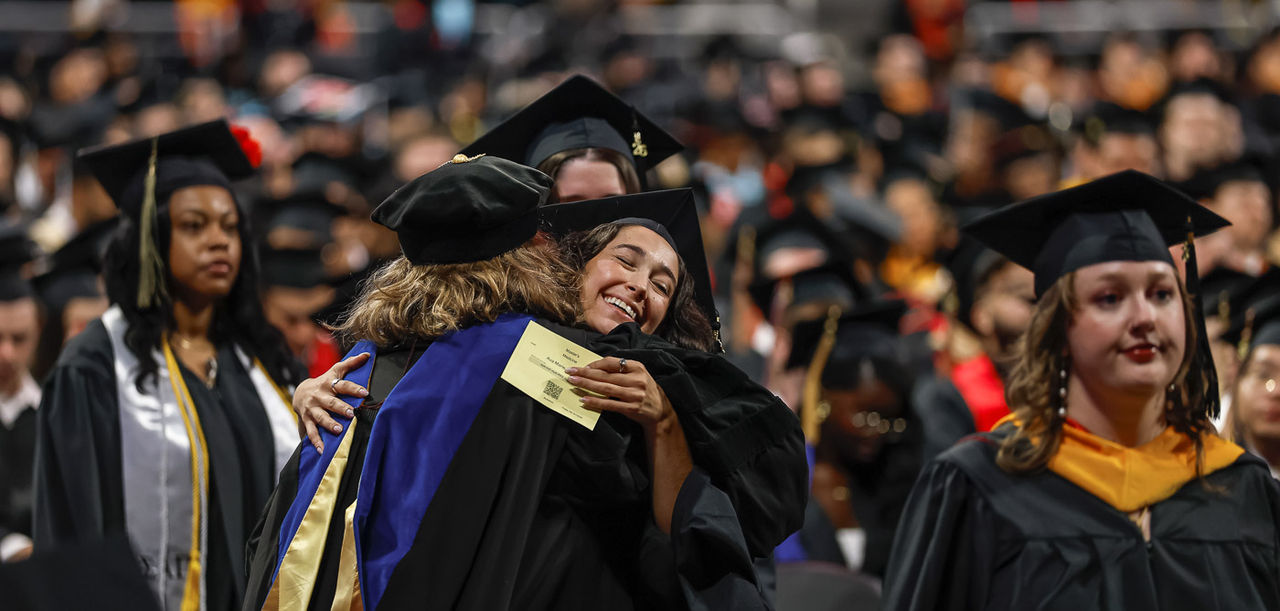  A grad in a cap and gown hugs a faculty member on the floor of Fifth Third Arena.