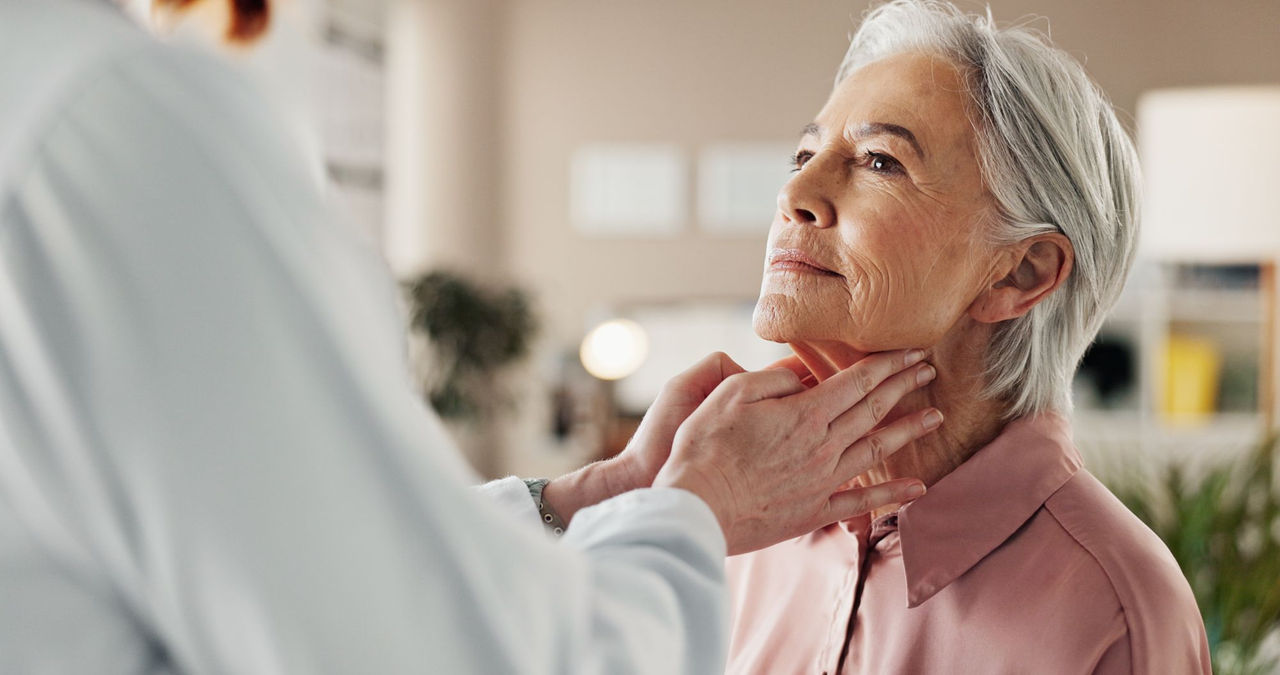 Doctor places hands on lymph nodes of elderly woman patient