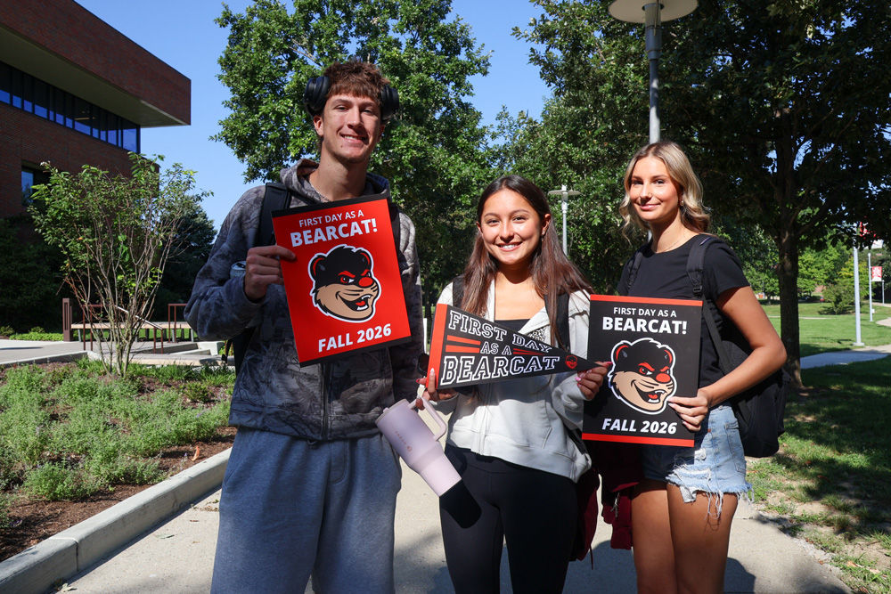 three students holding Bearcat signs outside on the UC Blue Ash campus