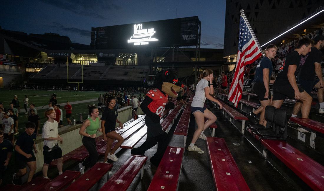 Students including one carrying an American flag run the stairs of Nippert Stadium. 