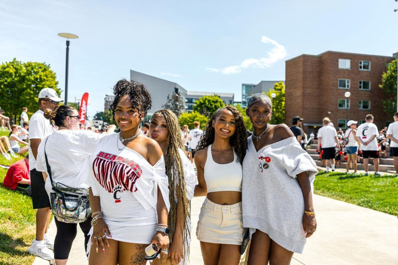 Four young women, excited Bearcats, smile for the camera and show off UC swag