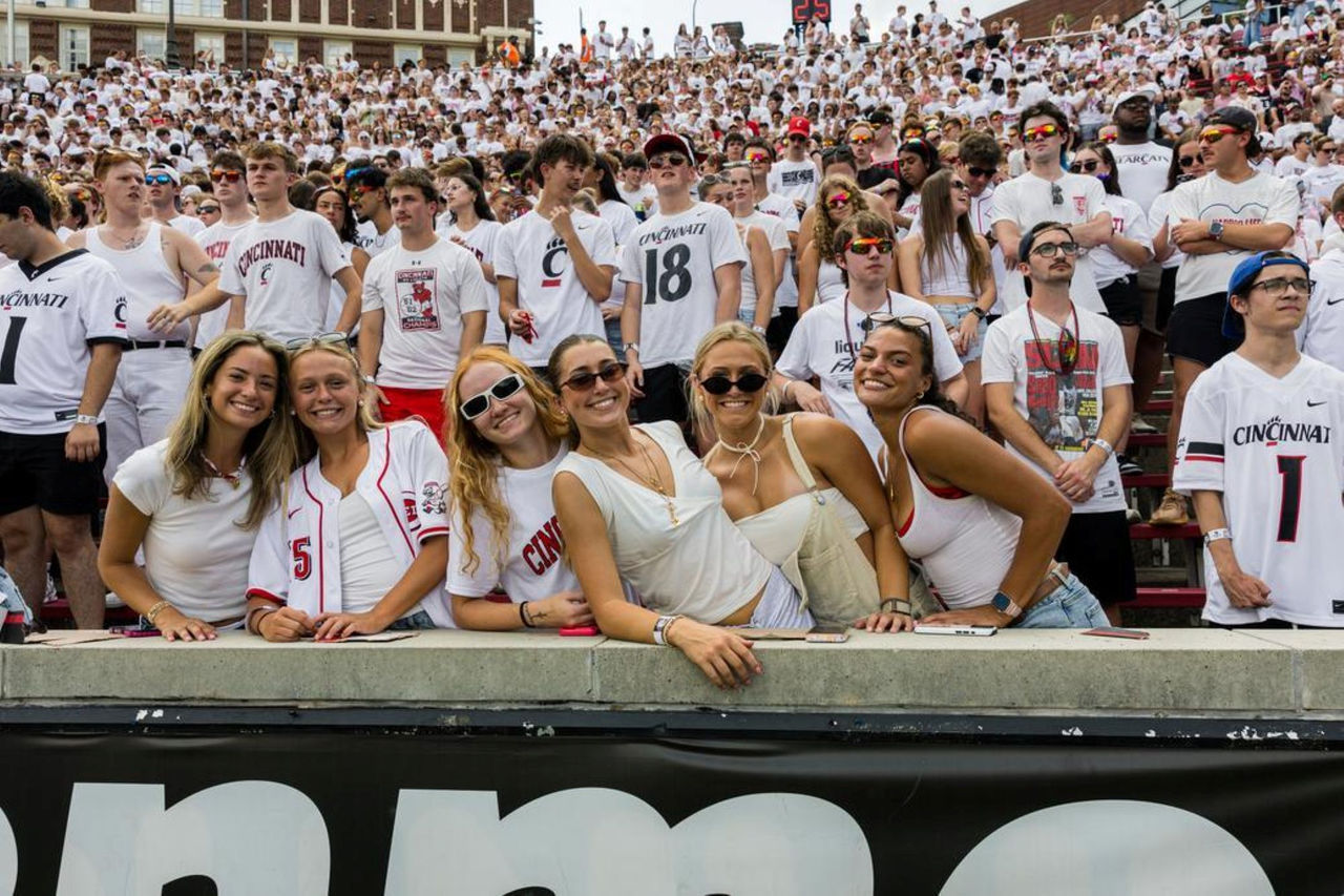 Hundreds of fans in Nippert Stadium in the background as six young women smile for the camera