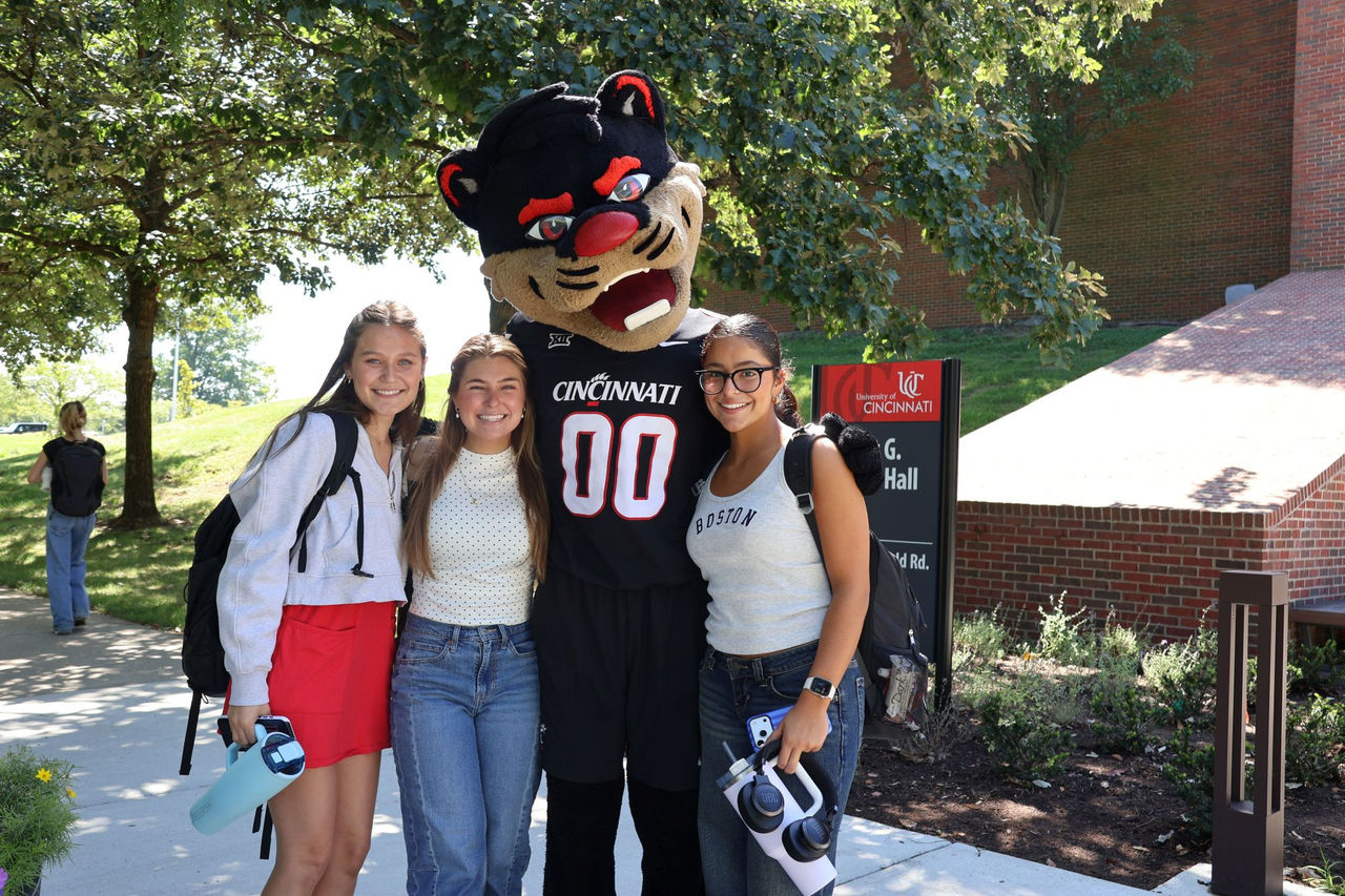UC bearcat mascot standing with three students outside of Muntz Hall on the UC Blue Ash campus