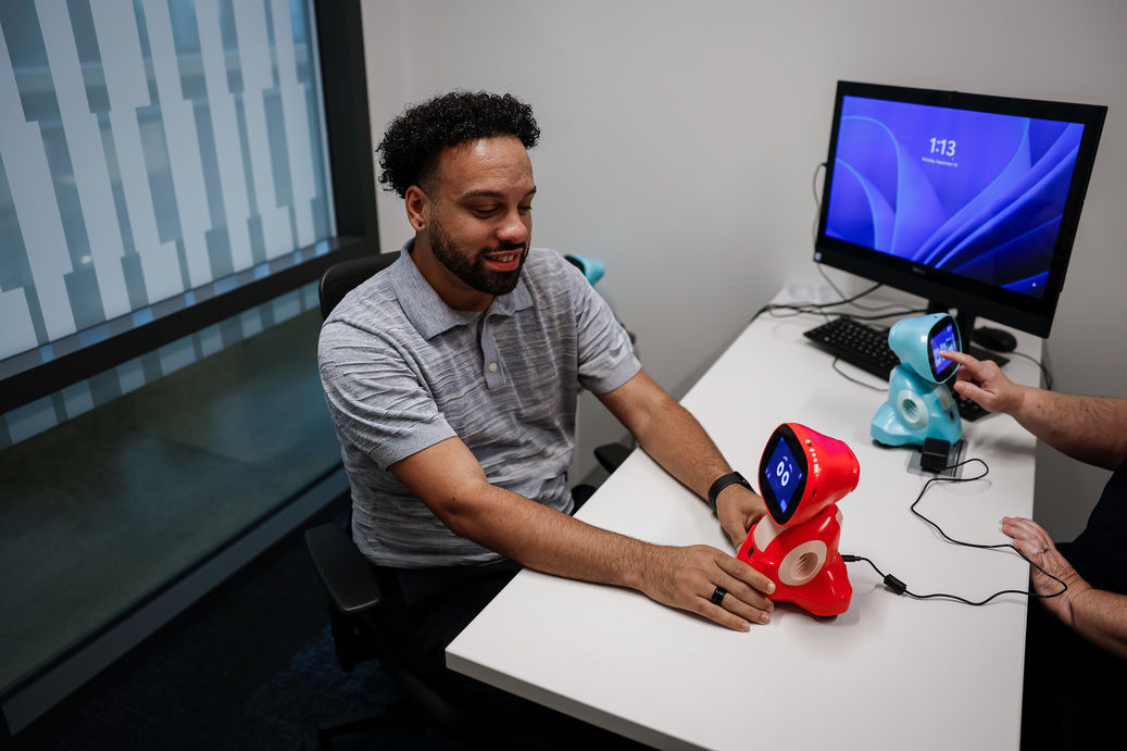 Kelly Merrill Jr. works with a toy robot that uses generative AI on a desk in an office.