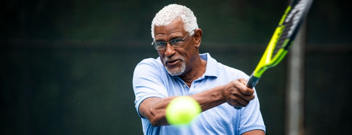 An elderly man hits a tennis ball with a racket