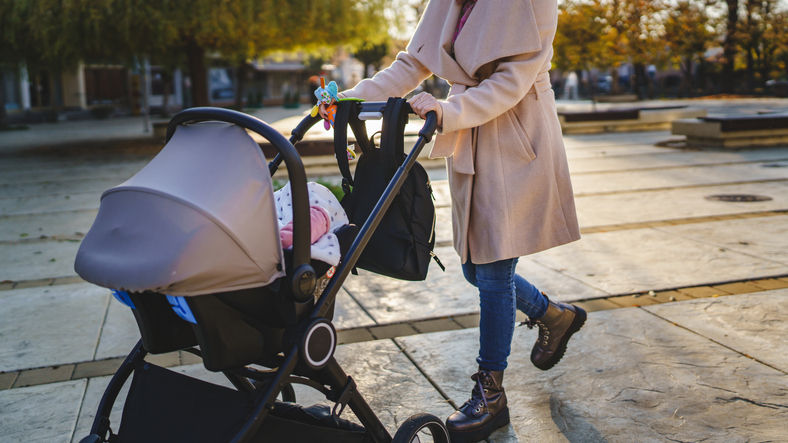 A woman pushes a baby in a stroller during the day in a city environment 