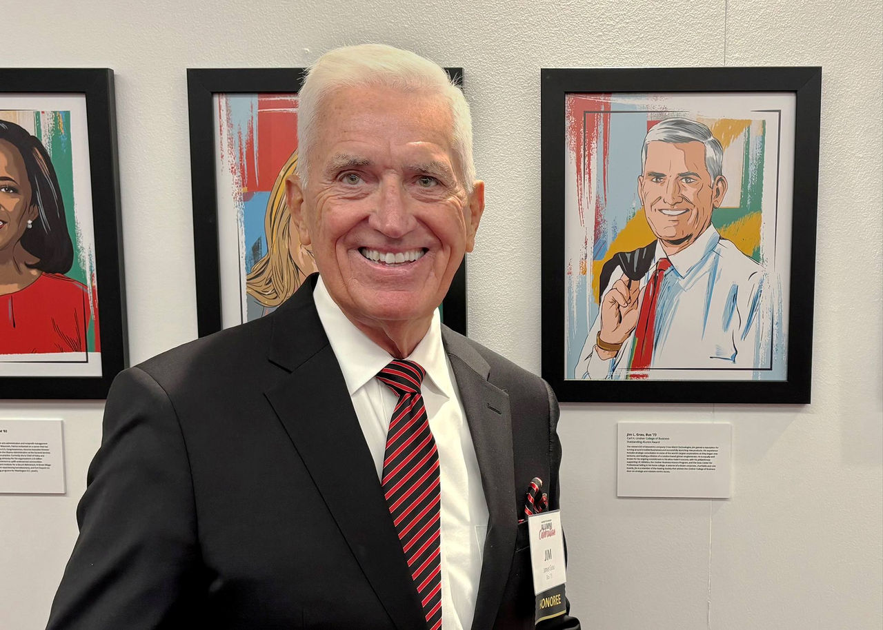 Jim Grau smiling in front of a drawing of him.