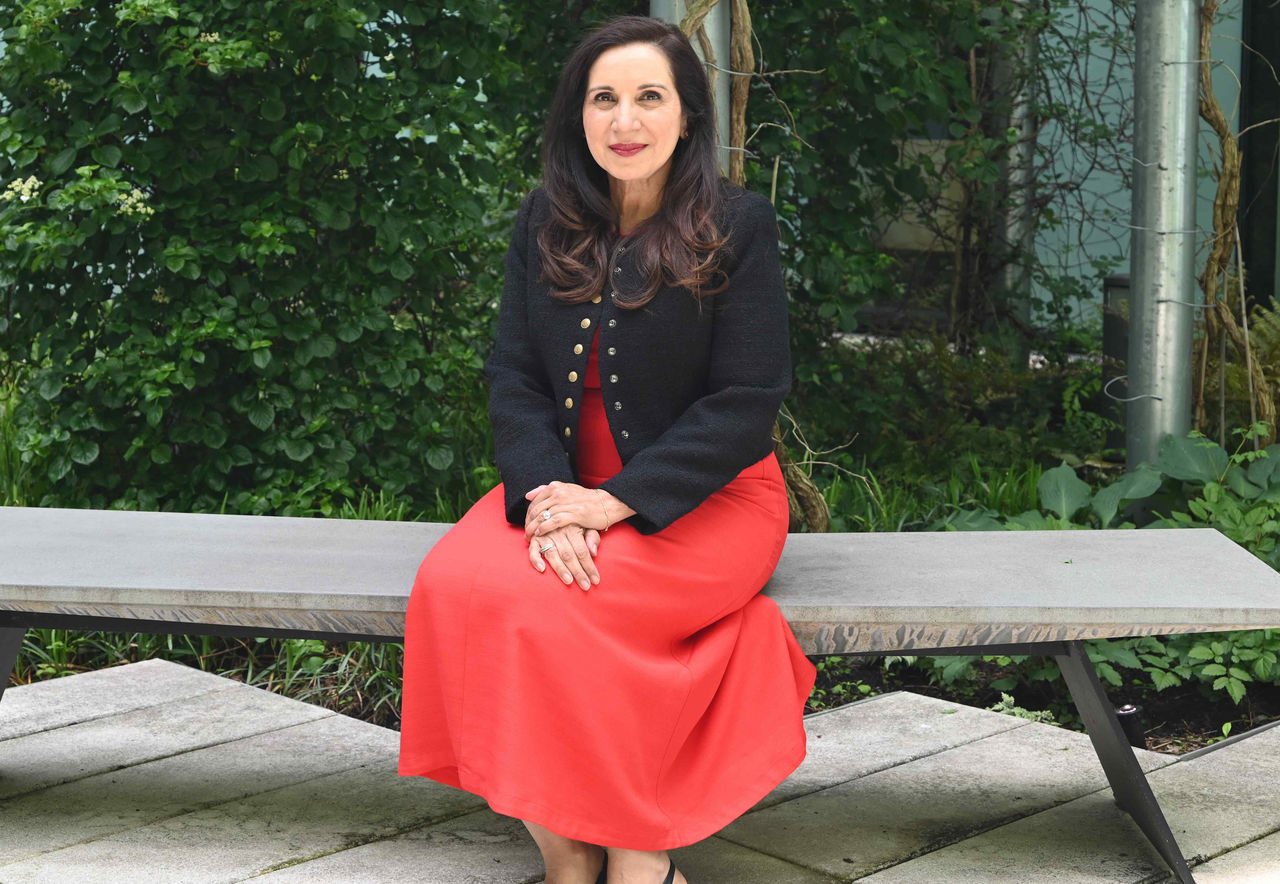  A woman in a red dress and dark top sits on a bench in a courtyard.