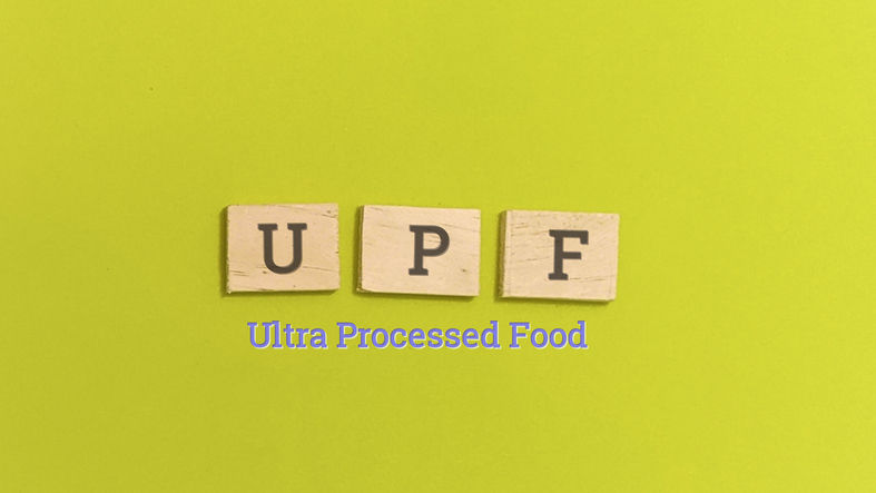 Wooden blocks of the letters "U", "P" and "F" on a green background with the words Ultra Processed Food below it