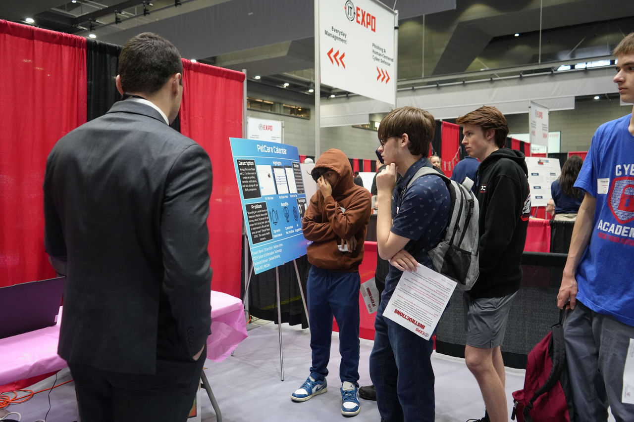 students speak with a person in a suit at an event