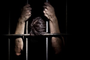 Man holding onto prison bars with head bowed.