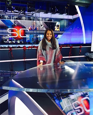 Taylor Jackson stands behind a newscaster's desk.