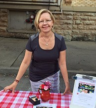 Theresia Marsh standing at a table with red checked tablecloth at a farmers market