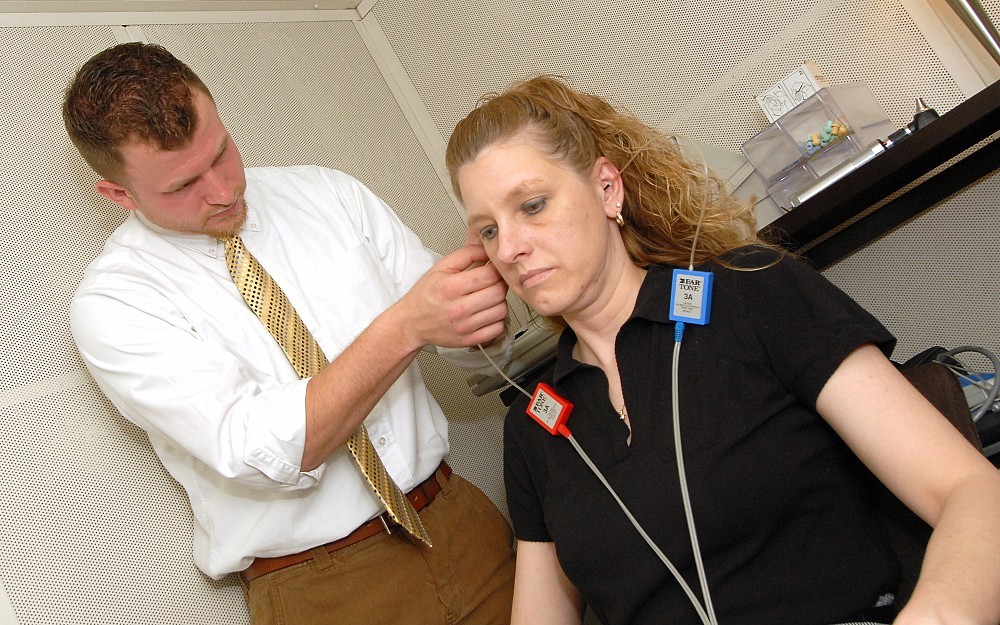 Part of the hearing screening test involves placing headphones or small ear plugs into the patientÂ s ear and instructing her to press a button upon hearing a beeping tone.