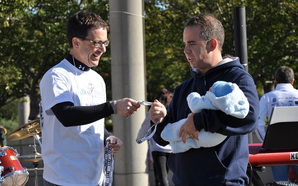Christopher McPherson, MD (right), receives his participation medal at the 2011 Walk Ahead for a Brain Tumor Cure run/walk Oct. 2, 2011, from Chris Knueven, an event co-chair and member of the Brain Tumor Center's Community Advisory Board. McPherson is holding his son, Alexander Christopher McPherson.