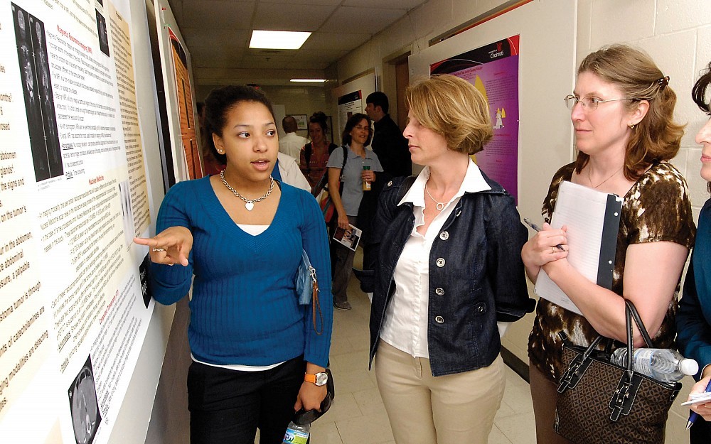 Student Jenifer Renfro (left) explains her research poster, Â The Use of Medical Imaging in Diagnosis of Neuroblastomas,Â  to PRaISE attendees Michelle Henlein and Cathleen Schweinfest.