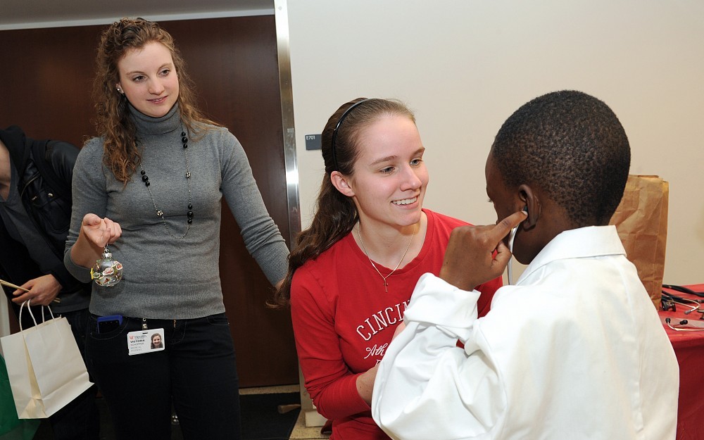 First-year medical students Victoria  Schopper (left) and Emily Hautman (right) help a student at the College of Medicine Holiday Festival discover what it's like to dress like a doctor.
