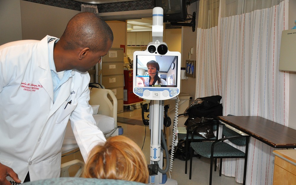 Opeolu Adeoye, MD, director of the Telestroke Program at UC Health University Hospital, demonstrates the technology. UC Health neurologist Dawn Kleindorfer, MD, is shown on the robot's monittor.