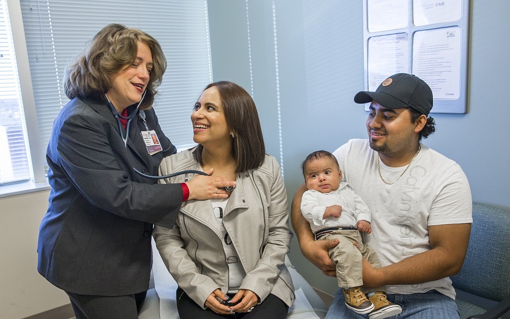 Stephanie Dunlap, DO, associate professor at the UC College of Medicine and UC Health physician, examines Lesly Maytee Samayoa Solares, while her husband Jonathan and their six-month-old Julian, watch.