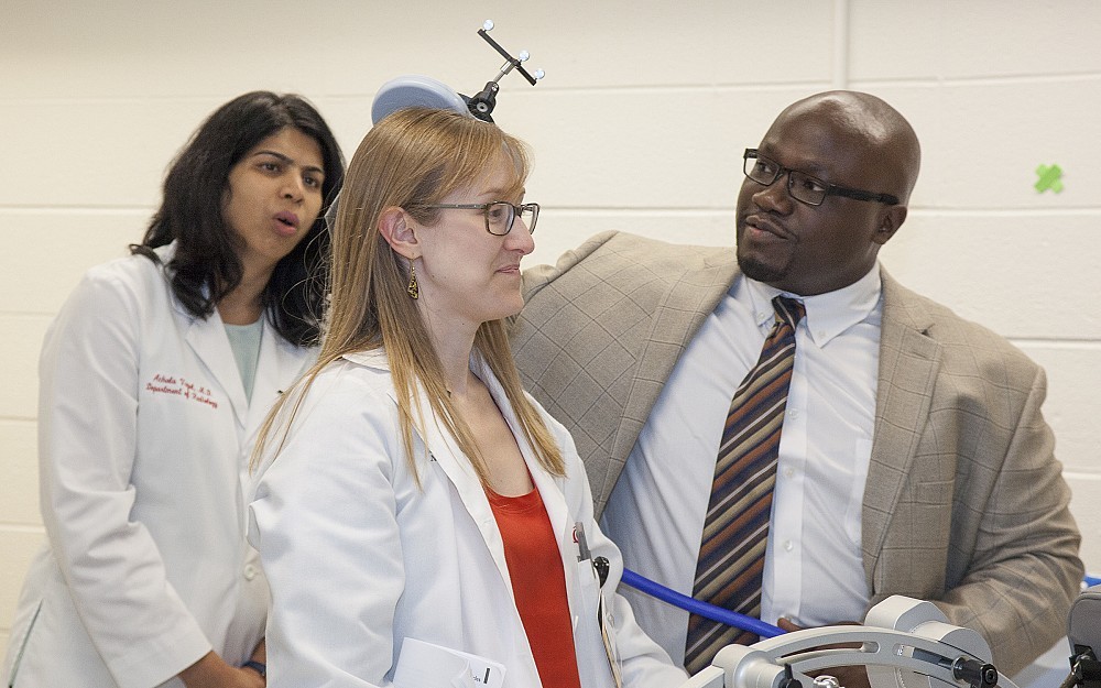 Oluwole Awosika, MD demonstrates the use of Transcranial Magnetic Stimulation (TMS) on colleague Elsiheva Coleman, MD. The device can be used to elicit movement of patient's arm or legs.