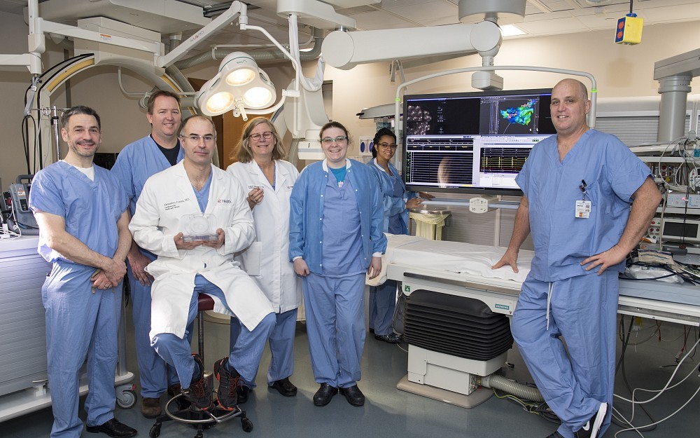 EP Lab Team shown from left to right: George Latus, Greg Maschinot, Alexandru Costea, MD, seated and holding Watchman Device, Laurie Vanderah, Emily Ruschman, Erin Evans (far rear) and Jonathan Groh.