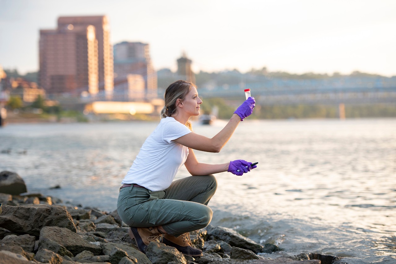 A UC student inspects a woter sample on the bank of the Ohio River