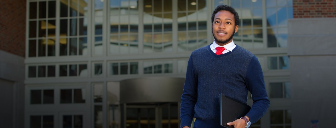 A UC student walks across campus carrying a laptop