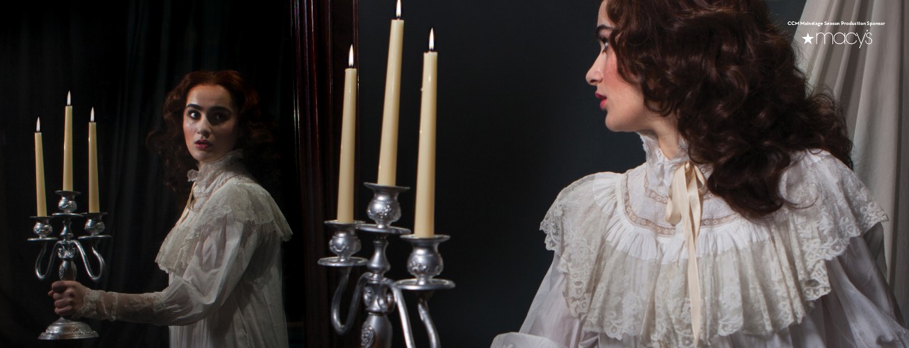 Woman in a nightgown holds a candelabra and looks into a mirror