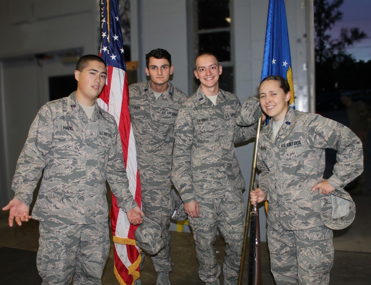 Fanning and three ROTC cadets posing with American flag, all in military camoflage attire. 