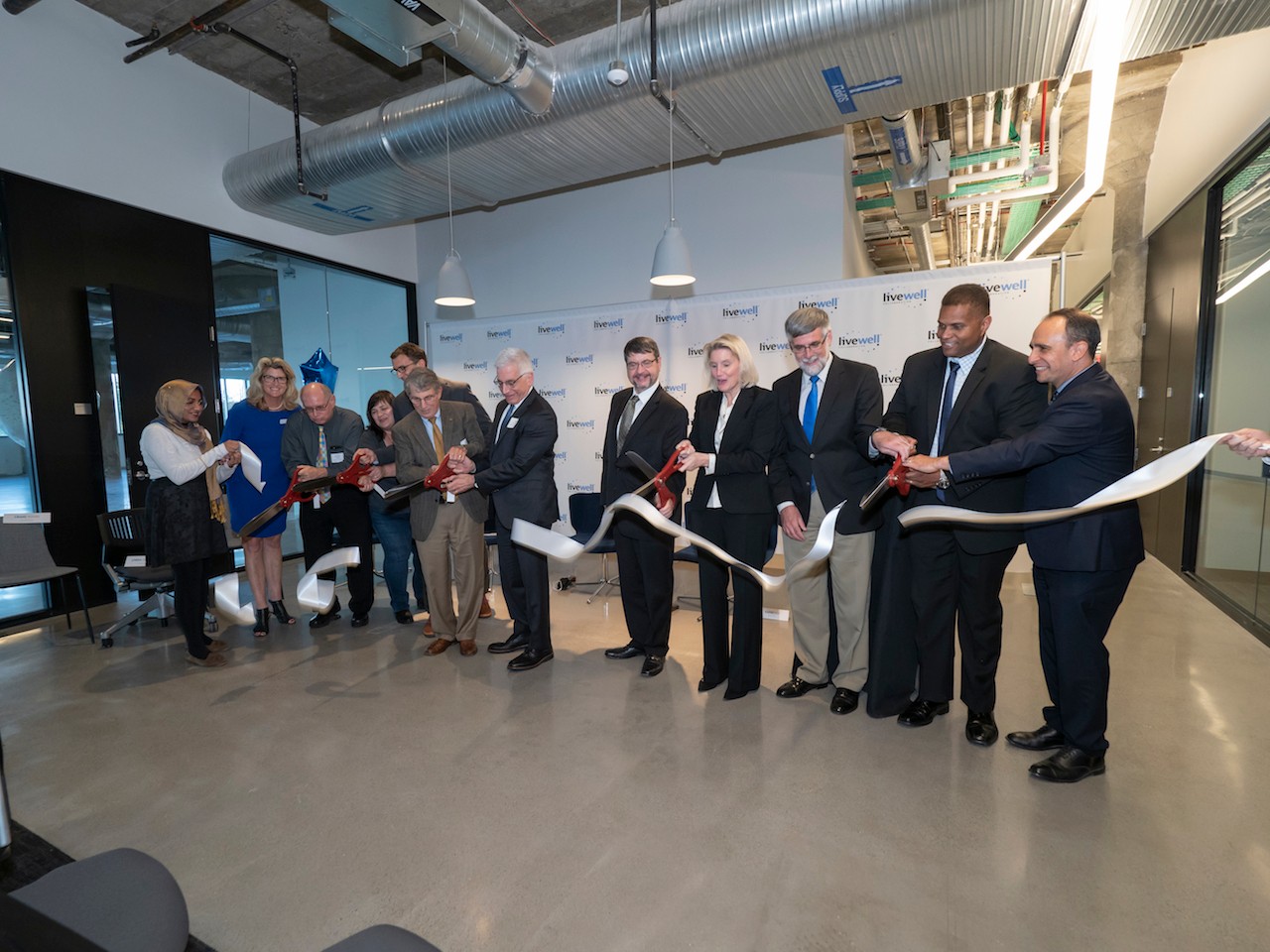 A line of people cut a ribbon with giant scissors at the LiveWell grand opening at the 1819 Innovation Hub