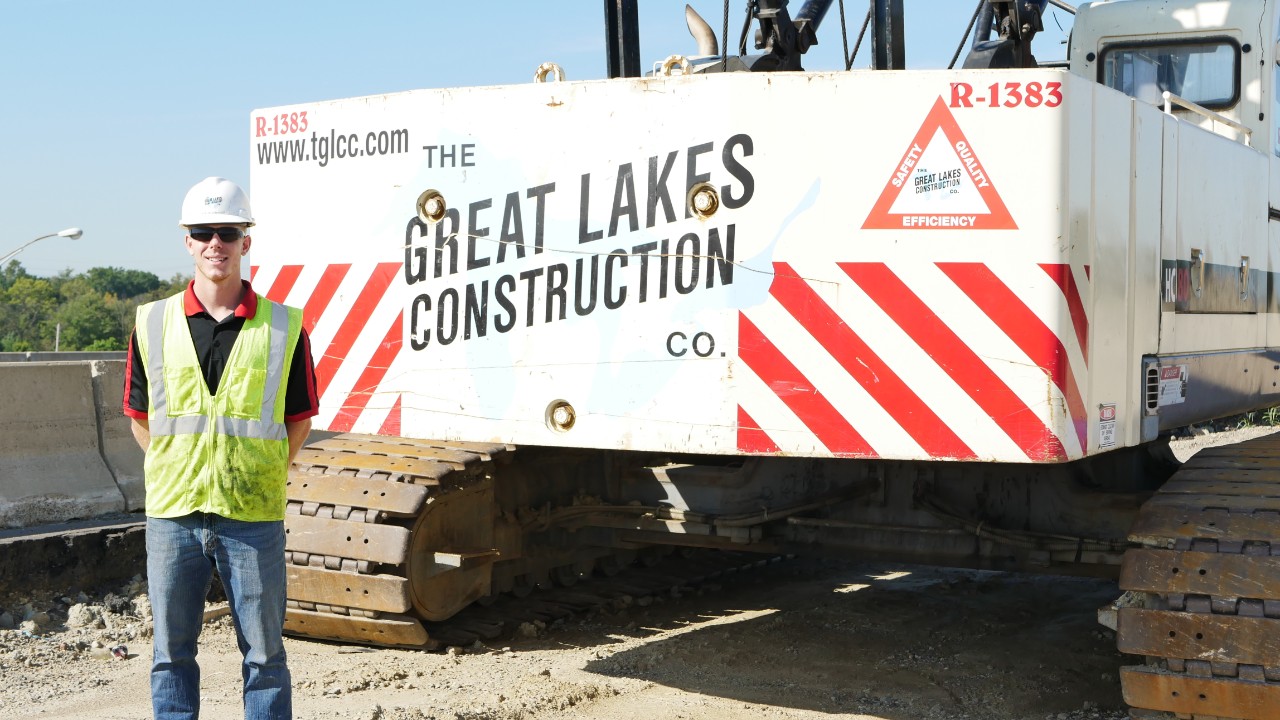 Niecwaner stands in front of construction vehicle. 