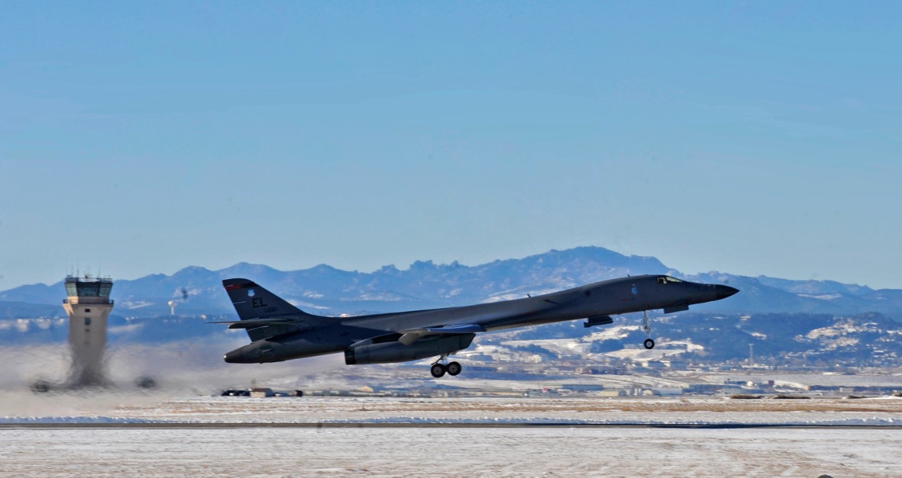 B-1B aircraft taking off with mountains in background. 