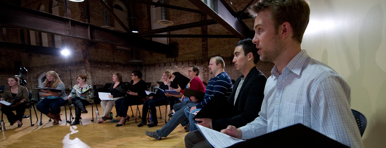 Singers sit in a circle with sheet music