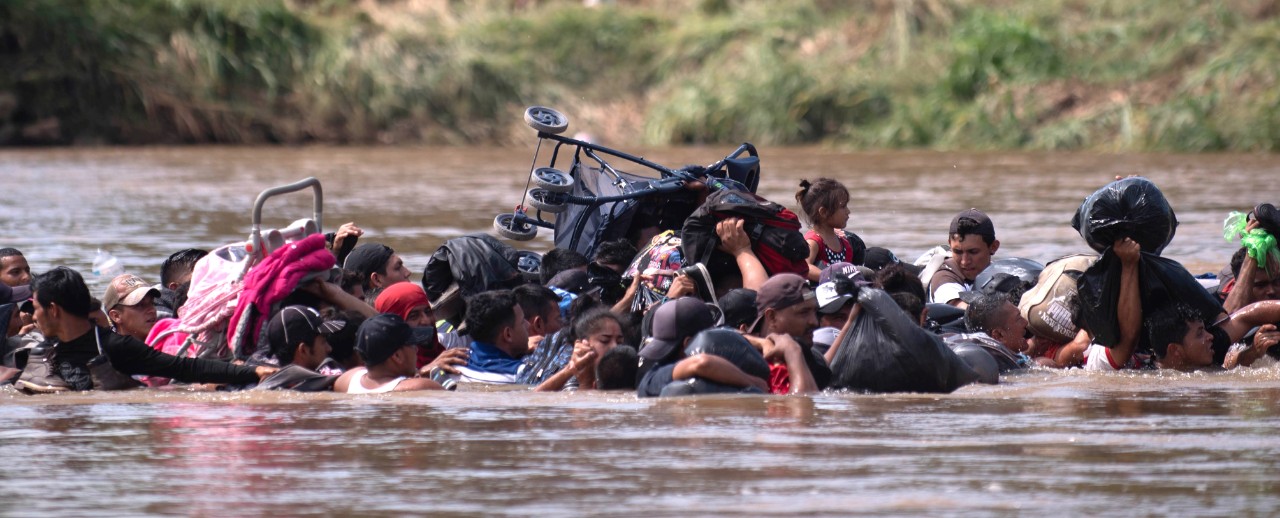 Migrants from Guatemala carry strollers and other belongings over their heads as they cross a deep river in Mexico.