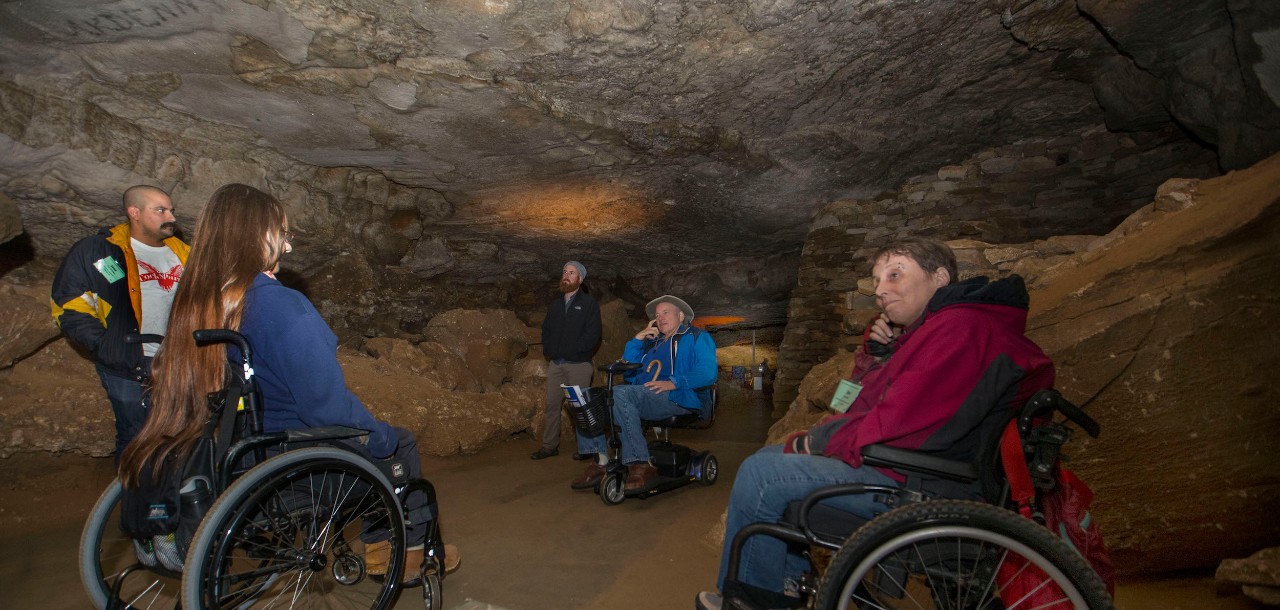 A woman in a wheelchair takes a picture of cave writings inside of Mammoth Cave