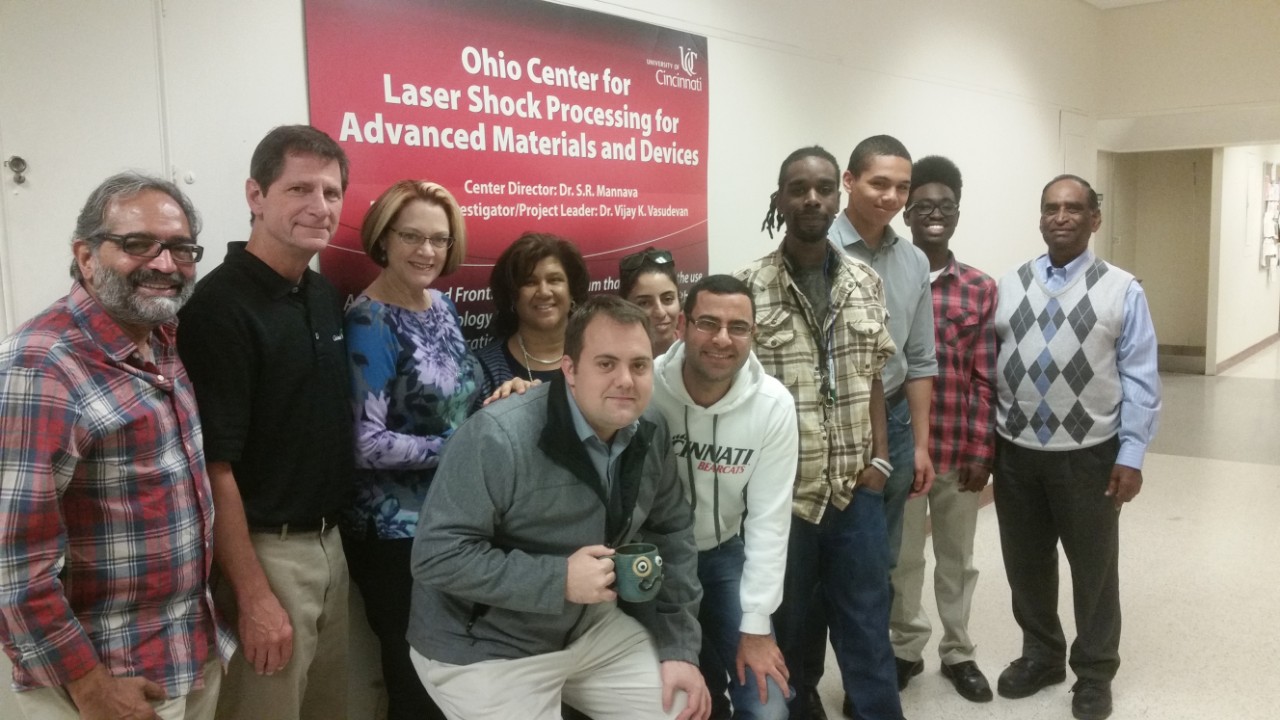 eleven people in casual and business casual clothing stand in front of a sign that says "Ohio Center for Laser Shock Processing for Advanced Materials and Devices"