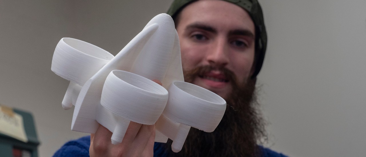 A member of UC Fly holds up a 3-D printed model of an early design for UC's flying car that resembles a rocket with fans for engines. 