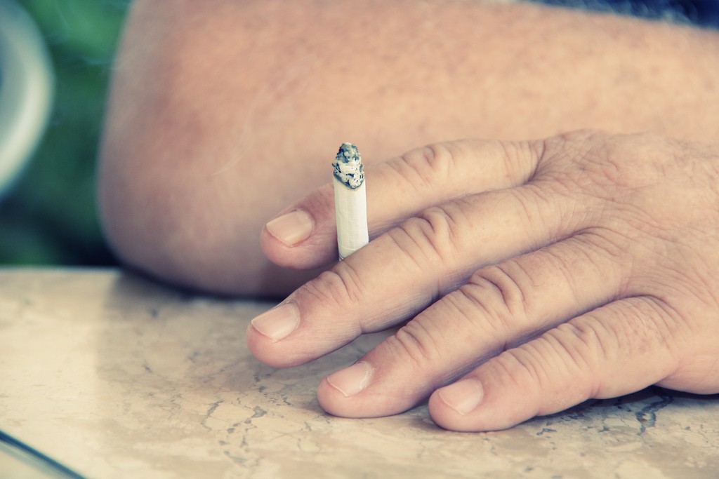 Close up of a hand holding a lit cigarette.